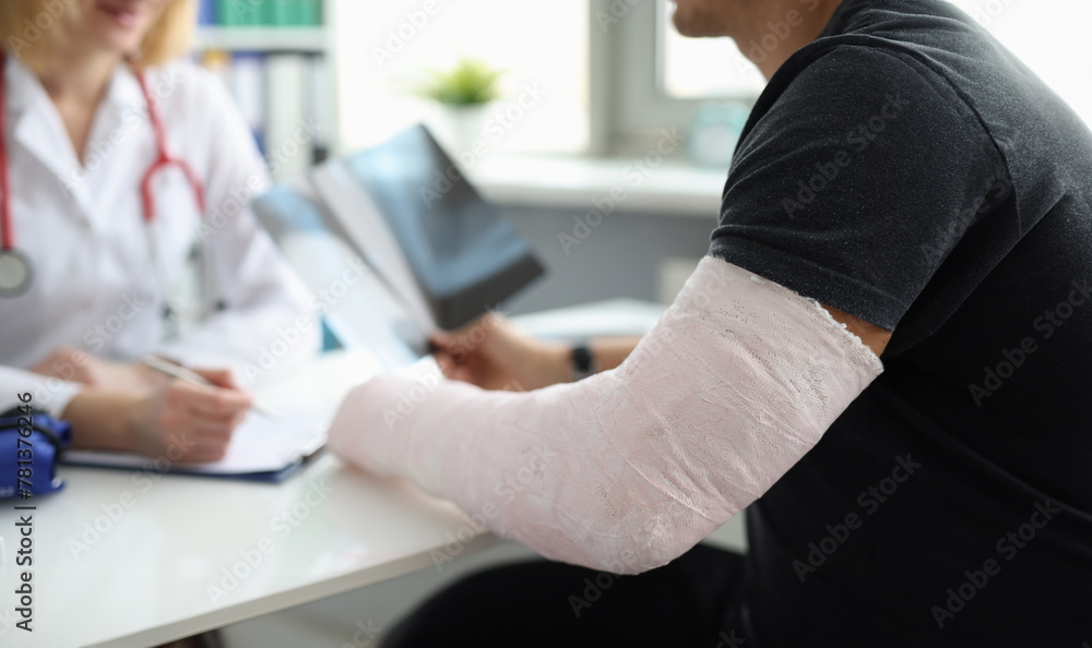 Doctor conducts medical consultation with patient with cast on arm. Hand fracture and treatment concept Doctor conducts medical consultation with patient with cast on arm. Hand fracture and treatment concept