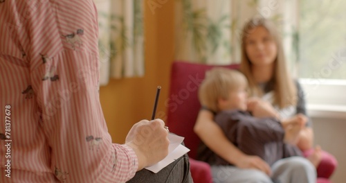 Woman with a child, hand in the foreground writing something on a piece of paper. Case worker or social worker meeting with client to discuss services, assistance, support provided by social services.