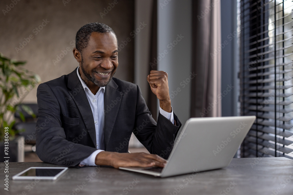 A man in a suit is sitting at a desk with a laptop and a tablet. He is smiling and he is happy A man in a suit is sitting at a desk with a laptop and a tablet. He is smiling and he is happy