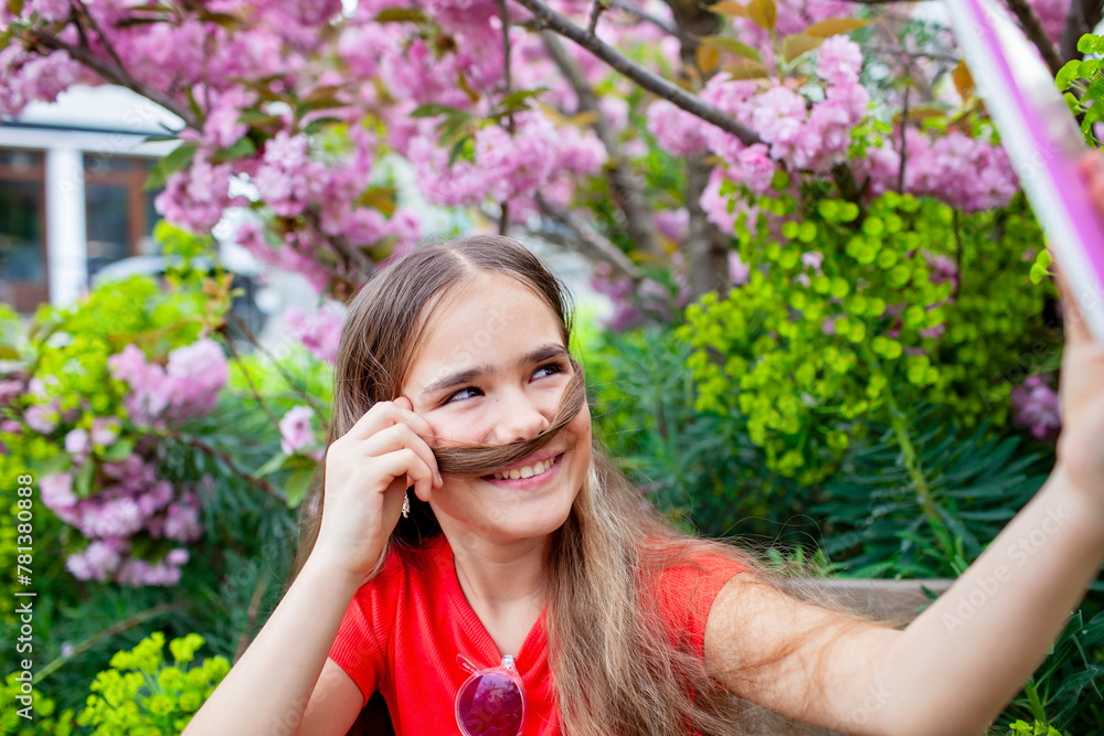 Girl using tablet under blossoming tree, sharing spring's beauty via video call, with playful hair mustache. Girl using tablet under blossoming tree, sharing spring's beauty via video call, with playful hair mustache.