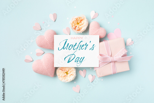 Festive background for Mothers Day. Paper card, hearts, rose flowers and gift box on blue table top view.