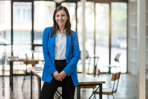 A professional woman with a confident smile stands in a bright, airy office space, dressed in a smart blue blazer with arms crossed.