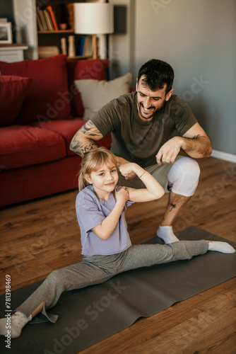 Father and daughter engaged in homework together, clad in sporty attire, in a vibrant modern living room © La Famiglia