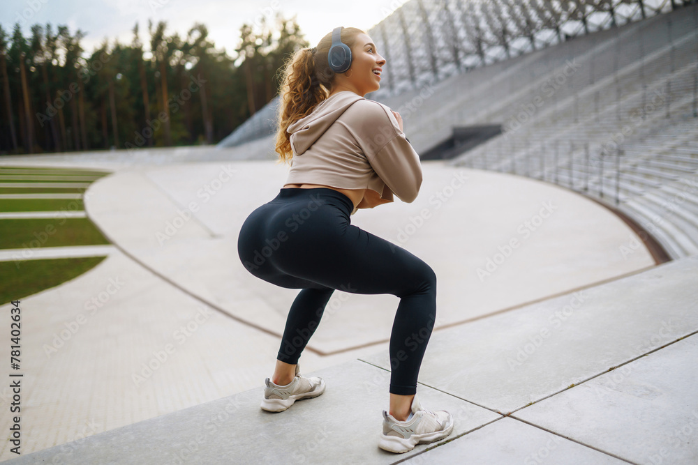 Fototapeta premium Smiling young woman doing morning gymnastics outdoors. Active life, sports training, healthy lifestyle