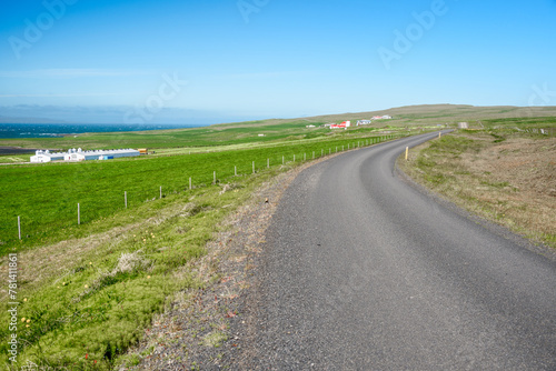 Desertefd back road through a rural landscape with grassy fields and farm buildings in Iceland on a sunny summer day