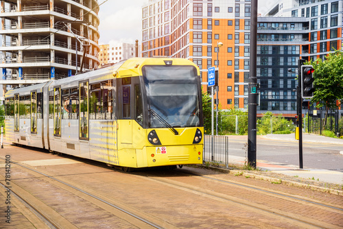 Yellow tram on a tramway running through a new suburban residental district on a sunny summer day. An apartment building under construction is in background.