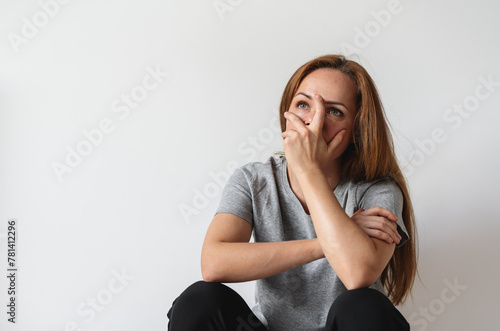Unhappy depressed woman sits next to grey wall covers face with her hand. PTSD.