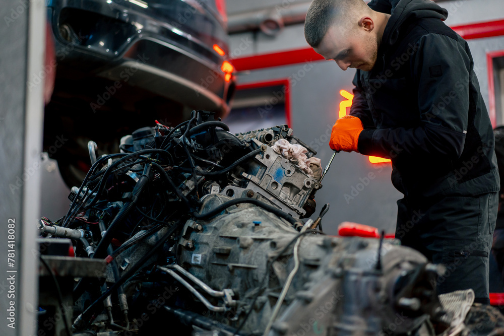 Fototapeta premium At a service station young master repairs a motor part removed from a car for a complete overhaul