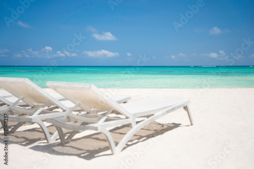 Beautiful view of tropical beach with white sand and turquoise sea water through empty sun loungers without people. The best summer vacations ideas and destinations. Caribbean copy space background 