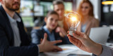 A hand holding a light bulb with business people in an office brainstorming meeting. A creative team or group with Innovative business idea.