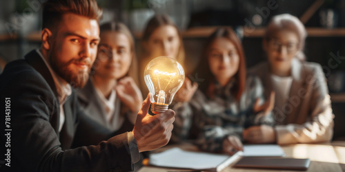 A man's hand holding a light bulb with business people in an office brainstorming meeting. A creative team or group with Innovation, business idea. photo