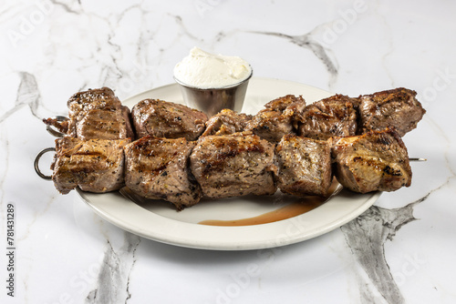 Two skeweres of lamb souvlaki on a plate with a serving of Greek Tzaziki photo