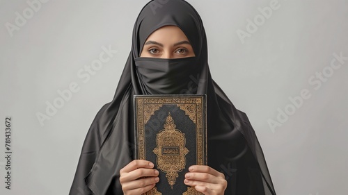 Happy Saudi Muslim woman wearing a black chador and holding a copy of the Holy Quran, isolated on white in a portrait