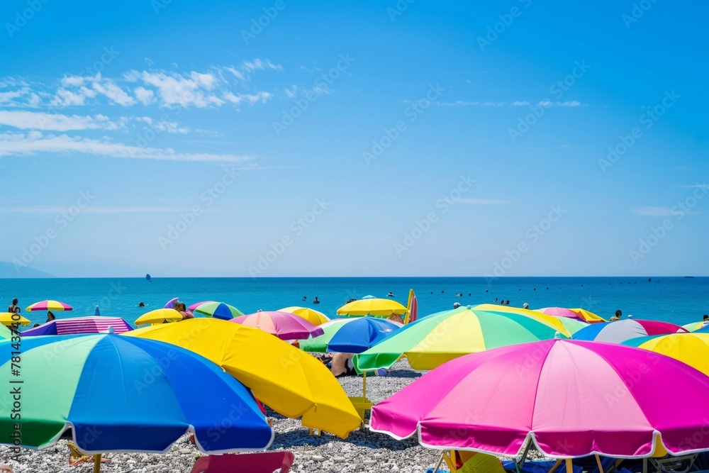 A beach scene with many colorful umbrellas and people enjoying the sun. Scene is cheerful and lively