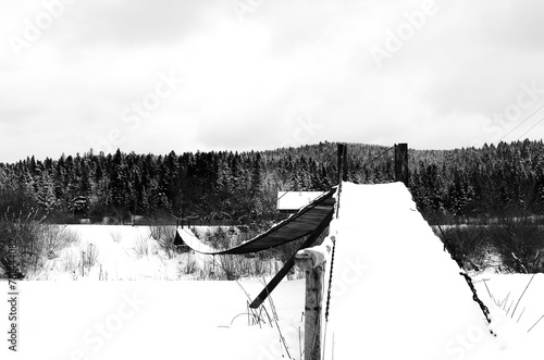 Lviv Oblast / Ukraine: Wintry impression of a small snow covered simple suspension bridge over the river Strwiaz photo