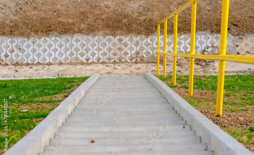 Świeżo zbudowane betonowe schody z żółtą stalową poręczą. Betonowe schody prowadzące w dół zbocza na skraju nowo wybudowanej drogi. © Grzegorz