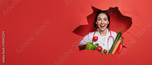 An excited chef woman showcases a variety of colorful vegetables, popping through a red paper backdrop © Fxquadro