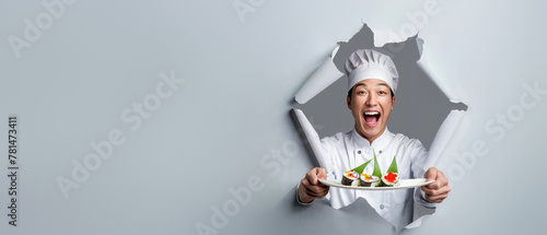 A happy chef in a white toque pops through a grey paper background, presenting a dessert plate