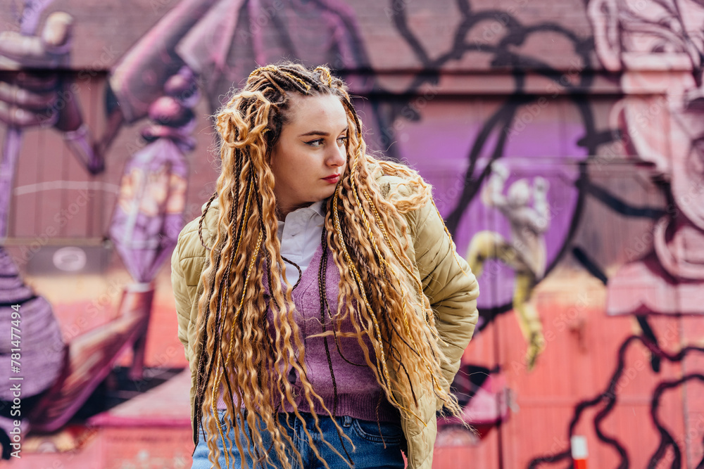 Naklejka premium Effervescent energy meets urban chic as a vibrant young woman poses against a backdrop of colorful graffiti-filled walls