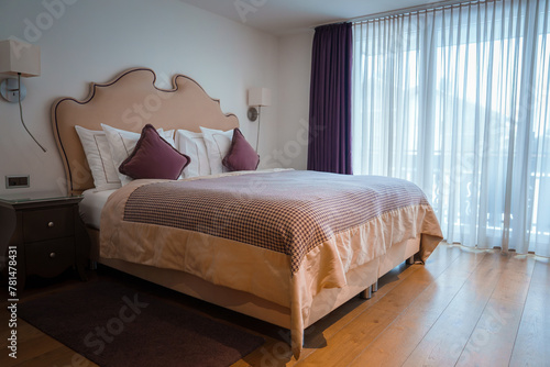 Luxurious hotel room in Zermatt  Switzerland. Large bed with elegant headboard  white linens  checkered bedspread  hardwood floors  warm color accents.