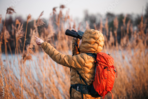 Woman naturalist with binoculars is looking for animals and birds at lake. Bird watching and wildlife observation. Eco tourism photo