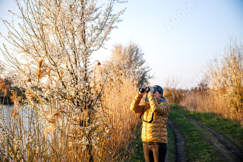 Bird watching. Woman ornithologist with binoculars observes birds arriving at lake in spring © encierro