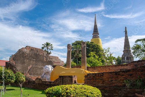 Historic site in Thailand featuring a reclining Buddha statue, ancient stupas, and weathered brick walls amidst tropical flora..