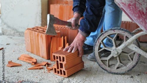 The rugged work at a construction site as a worker trims bricks using an axe, chipping off pieces with precision and skill.