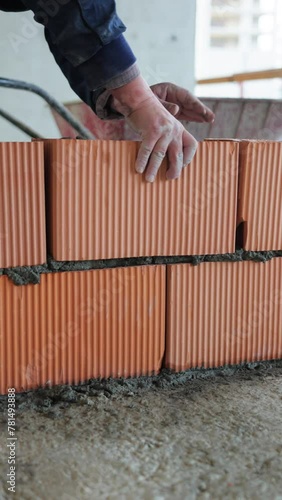 A builder adding a red brick to a brick wall at a construction site, pressing it down for a secure fit. Detailed bricklaying action n vertical video format.