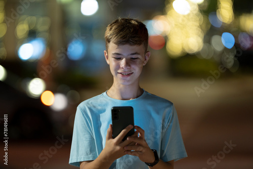 Happy teenage boy messaging on his cellphone outdoors at night photo