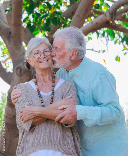 Portrait of tenderly senior couple hugging and kissing in outdoors public park under a big tree. Carefree lovely couple enjoying freedom and retirement #781503228