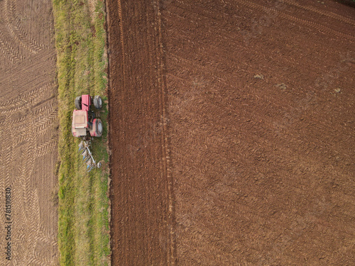 Aerial view of a red tractor plow the farmland 