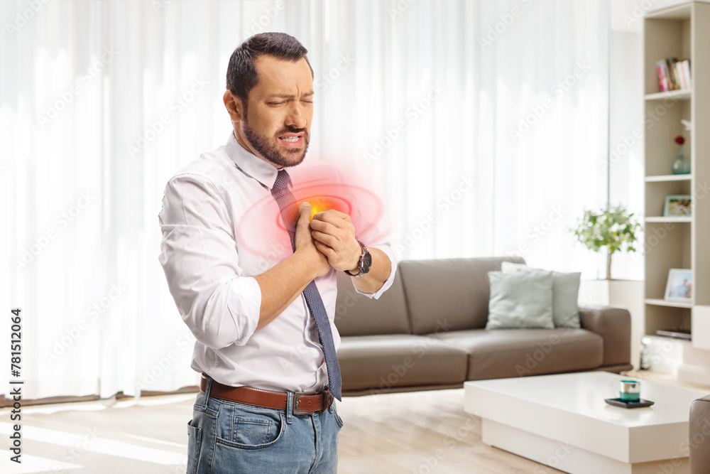 Businessman in a living room holding his chest in pain at home Businessman in a living room holding his chest in pain at home