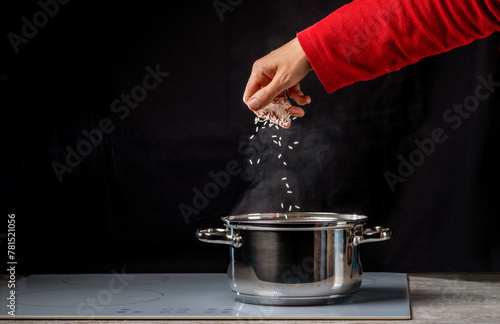 A woman's hand throws grains of rice into a pot of boiling water on the stove. Cooking food.