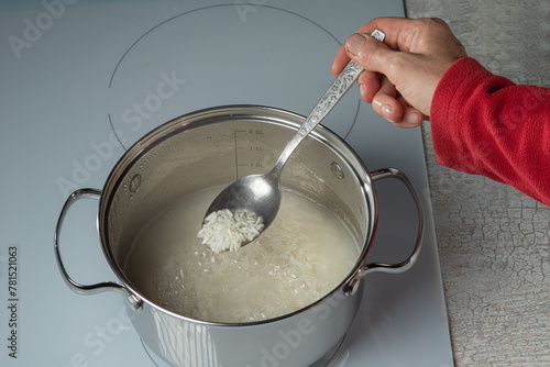A spoon with rice in a woman's hand over a pot of boiling rice. Selective focus.