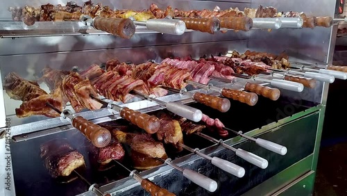 Grill with rotating skewers and drawer with embers: on different levels we see skewers of pork ribs, shanks and sausages rotating. You can see some smoke rising. Italian food and traditions. photo