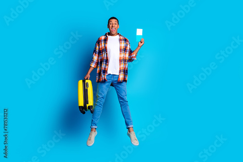 Full size photo of nice young man suitcase passport jump empty space wear shirt isolated on blue color background photo