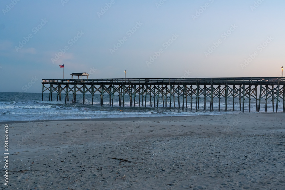 A wooden fishing pier at sunset with an American Flag at the end. Pawleys Island, South Carolina.