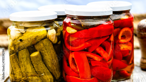 Glass jars with pickled red bell peppers and pickled cucumbers (pickles) isolated. Jars with variety of pickled vegetables. Preserved food concept in a rustic composition. © Vlad Ispas