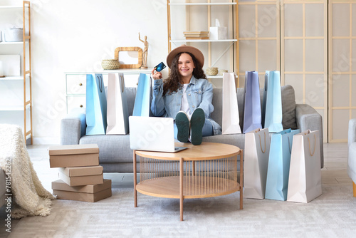 Young woman with laptop, credit card and bags shopping online at home