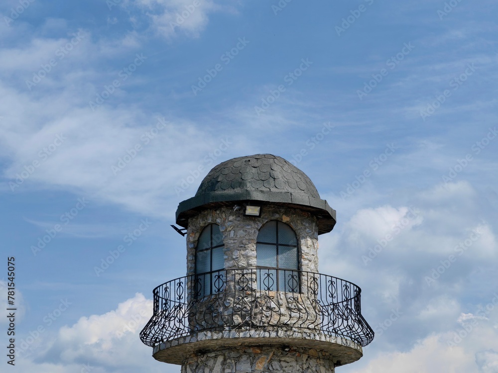 Top view, of the local tower. Building construction. Stone, material. Window frame. Black fence. Blue sky with clouds. Top view, of the local tower. Building construction. Stone, material. Window frame. Black fence. Blue sky with clouds.