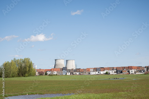 cooling tower chimneys from Vilvoorde industrial power plant outside Brussels Belgium above rooftops of residential skyline and green field area for public recreation on sunny blue sky day