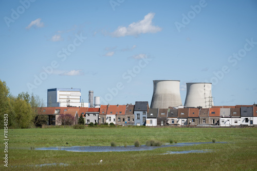 cooling tower chimneys from Vilvoorde industrial power plant outside Brussels Belgium above rooftops of residential skyline and green field area for public recreation on sunny blue sky day © drew