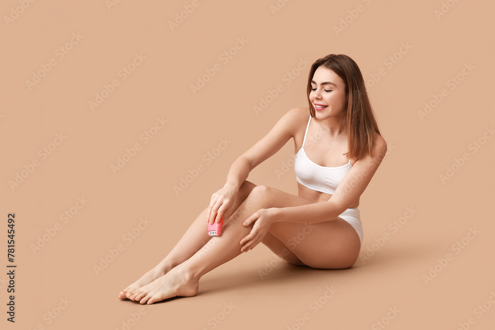 Beautiful young happy woman epilating her legs with modern epilator on brown background Beautiful young happy woman epilating her legs with modern epilator on brown background