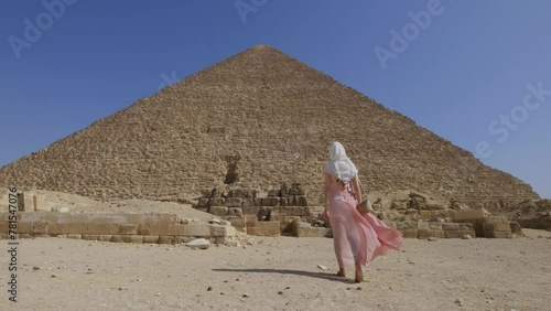 Back view of the young woman walking towards the Great Pyramids of Giza in Egypt. Tourist travel concept.