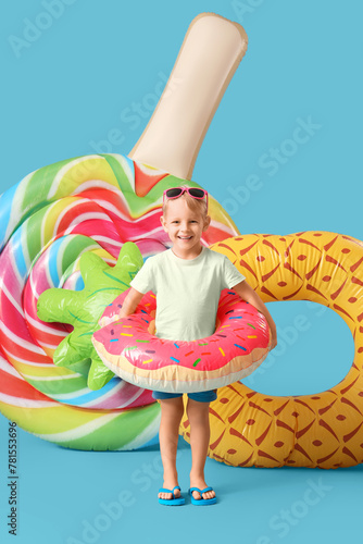 Cute little boy with swim rings and mattress on blue background