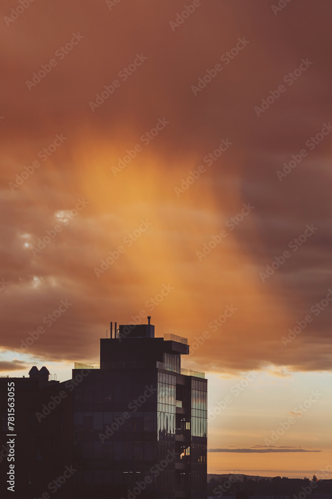 Fototapeta premium Sunrise clouds, some dark, some light up by the sun, over high rise buildings. Cityscape with wonderful fiery dawn. Amazing dramatic cloudy sky. Atmospheric background of sunrise in overcast weather.