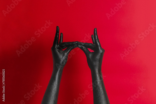 Black color painted woman's hands on her skin with red background. High Fashion art concept