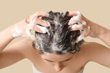 Beautiful young woman washing hair on beige background