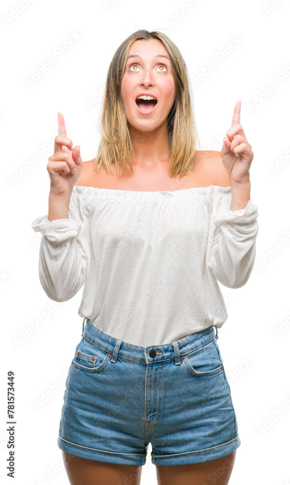 Young beautiful woman over isolated background amazed and surprised looking up and pointing with fingers and raised arms. Young beautiful woman over isolated background amazed and surprised looking up and pointing with fingers and raised arms.